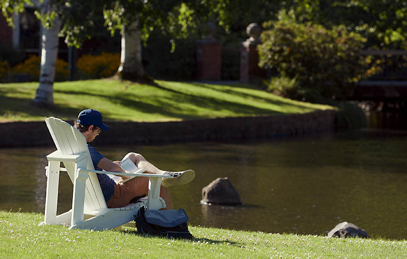 One person sitting in a lawn chair near green grass and the Mill Stream