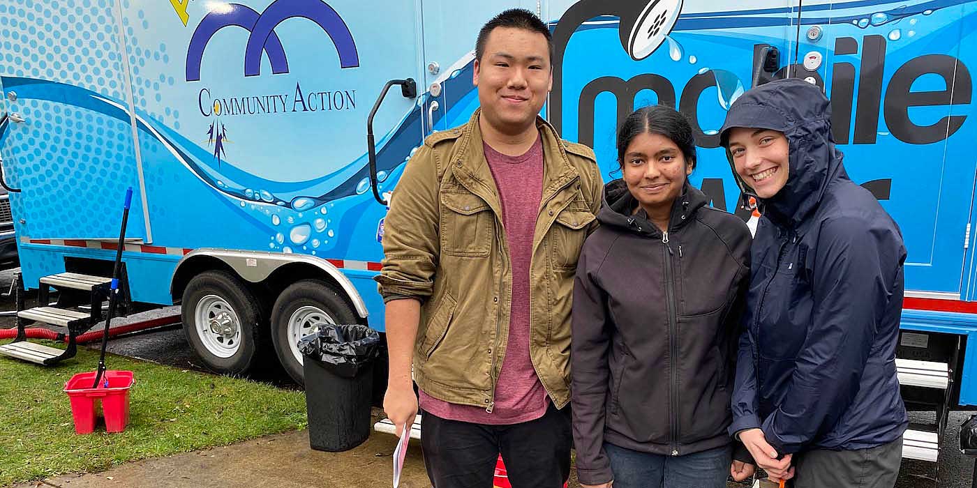 Three Public Health students volunteer at a community outreach event, standing in front of a mobile health services unit, showcasing hands-on learning and community engagement as part of their academic program.