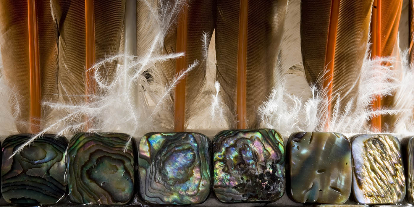 Closeup of a feathered headdress with abalone beads.