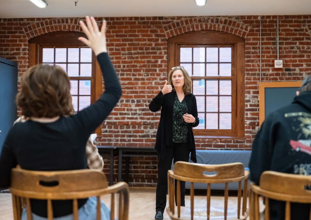 An instructor and a student with raised hand in a classroom setting.