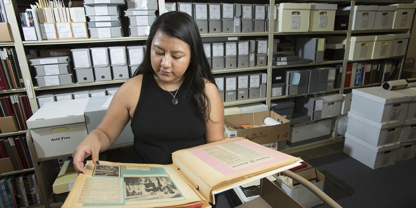 A Willamette student studies archival documents with shelves of archival materials in the background.