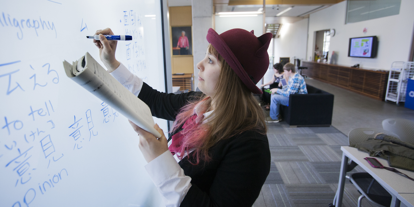 A student in a Japanese Studies academic program practices writing Japanese characters on a whiteboard, engaging in language learning and cultural studies at Willamette University.
