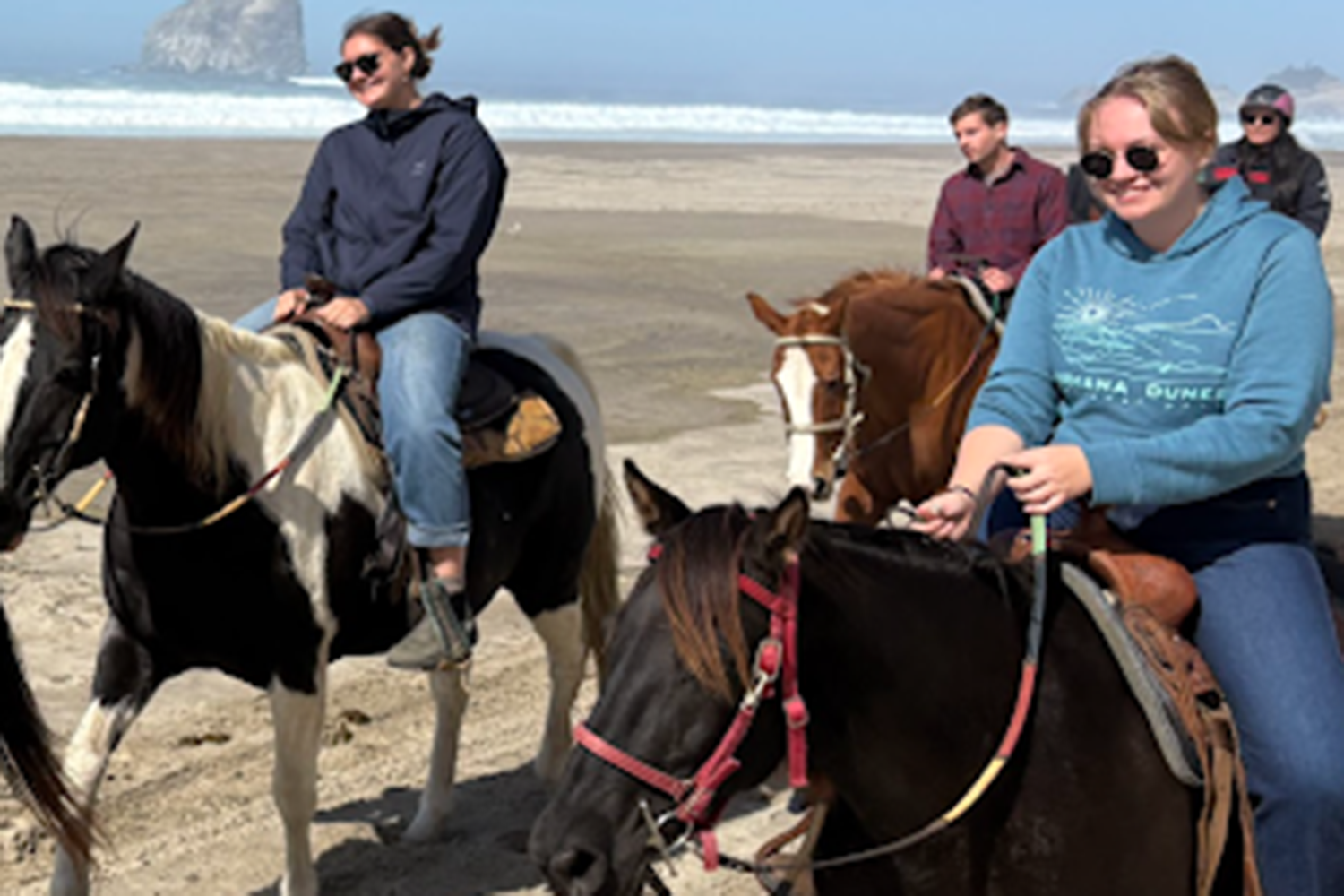 A group of students riding horses on a beach.