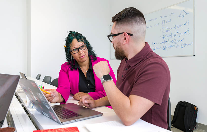 A professor in a blazer chatting with a student in a classroom
