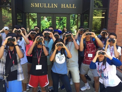 Students holding binoculars in front of Smullin Hall.