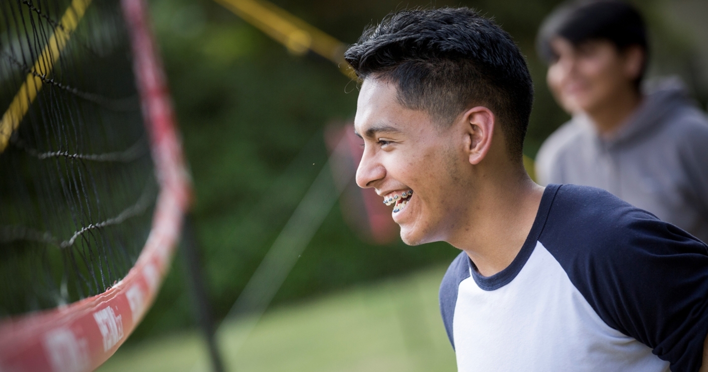 A student with braces smiling near a volleyball net
