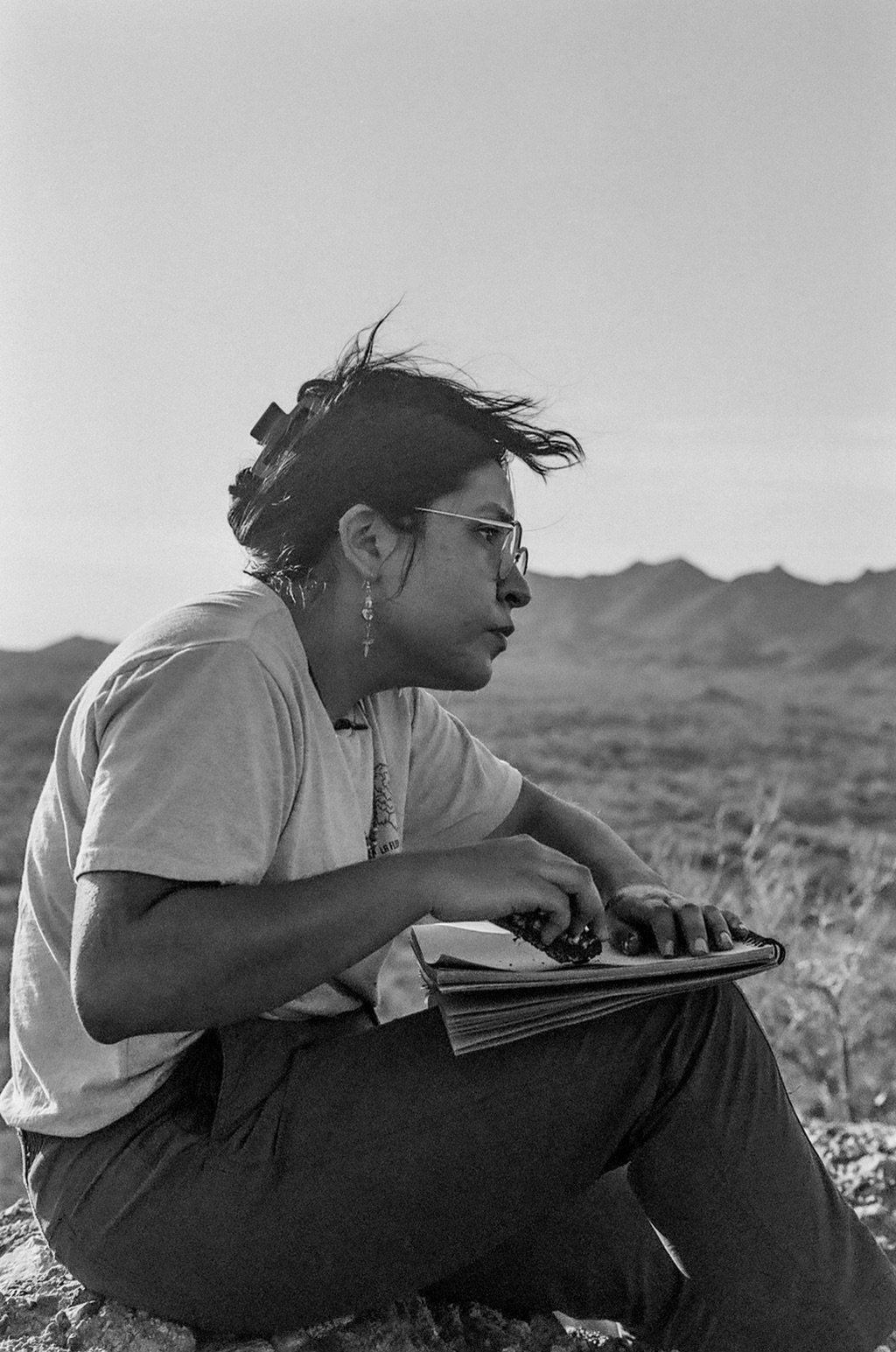 Yanely Rivas Maldonado sitting in a field with a sketchpad, mountains in the distance