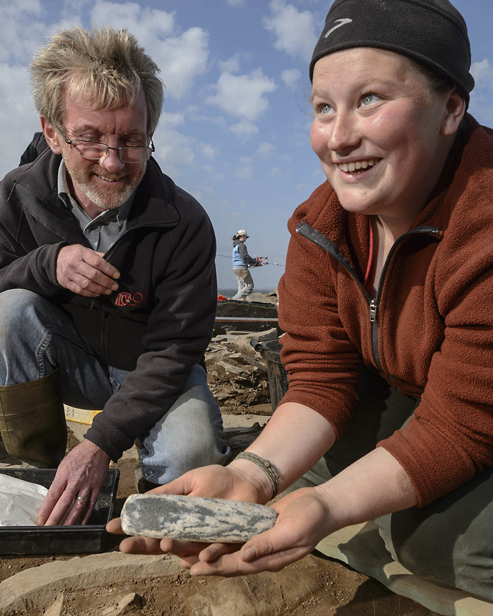 A student with a professor at a site holding a discovery