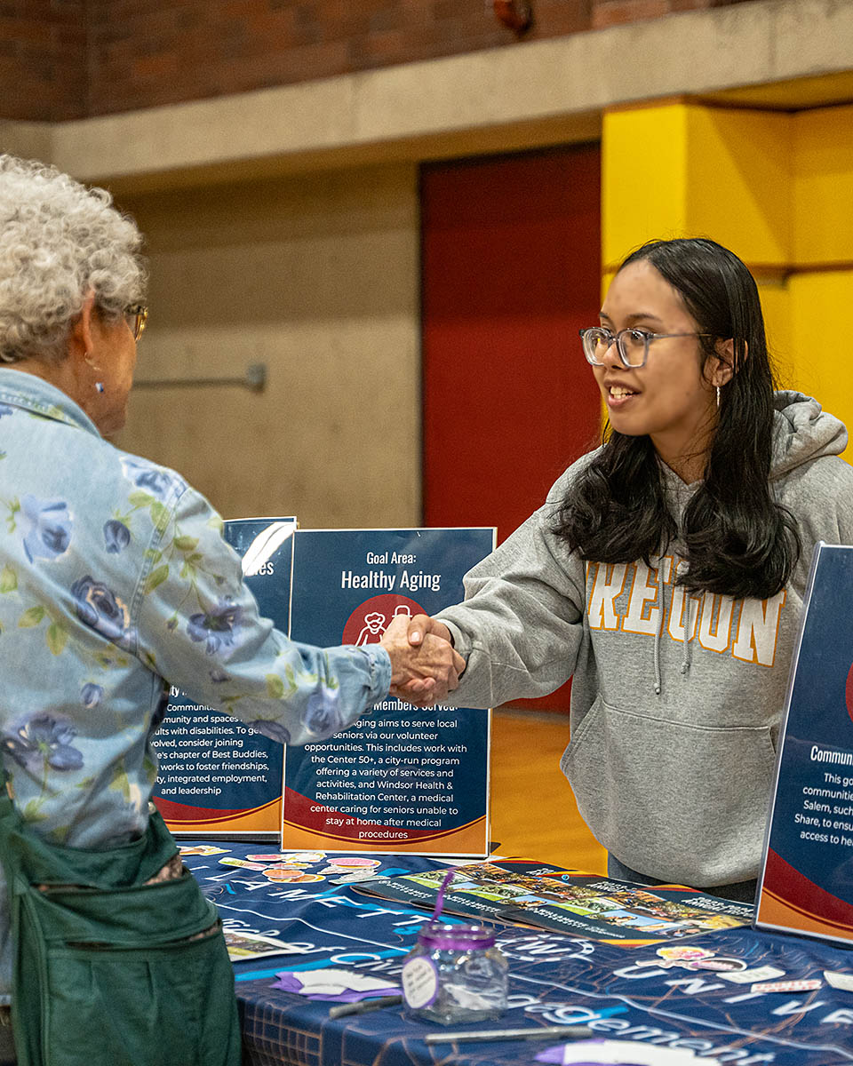 A Willamette student shakes a person's hand at a table with information about civic engagement