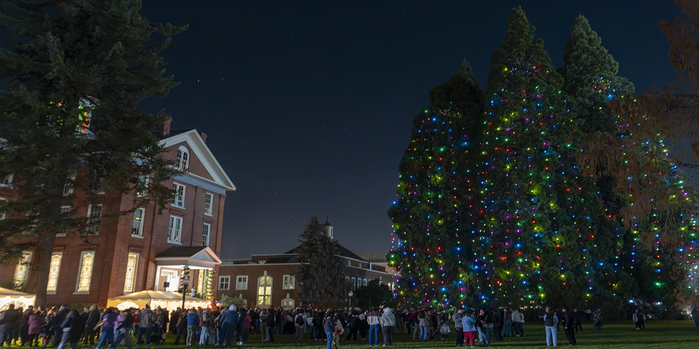Willamette's Star Trees with holiday lights, Waller Hall, and a group of people.