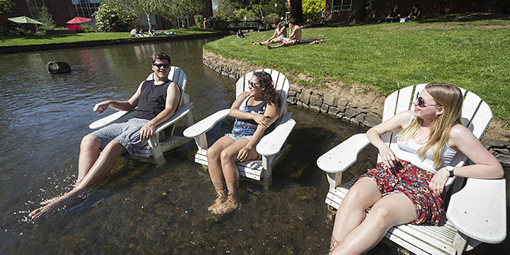 Three students sitting in lawn chairs in the river