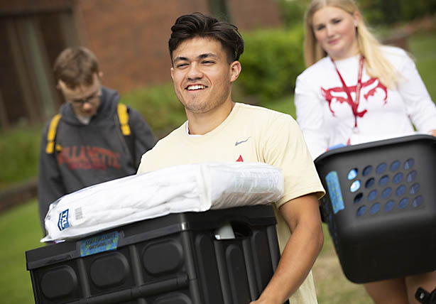 Three students carrying boxes to move in
