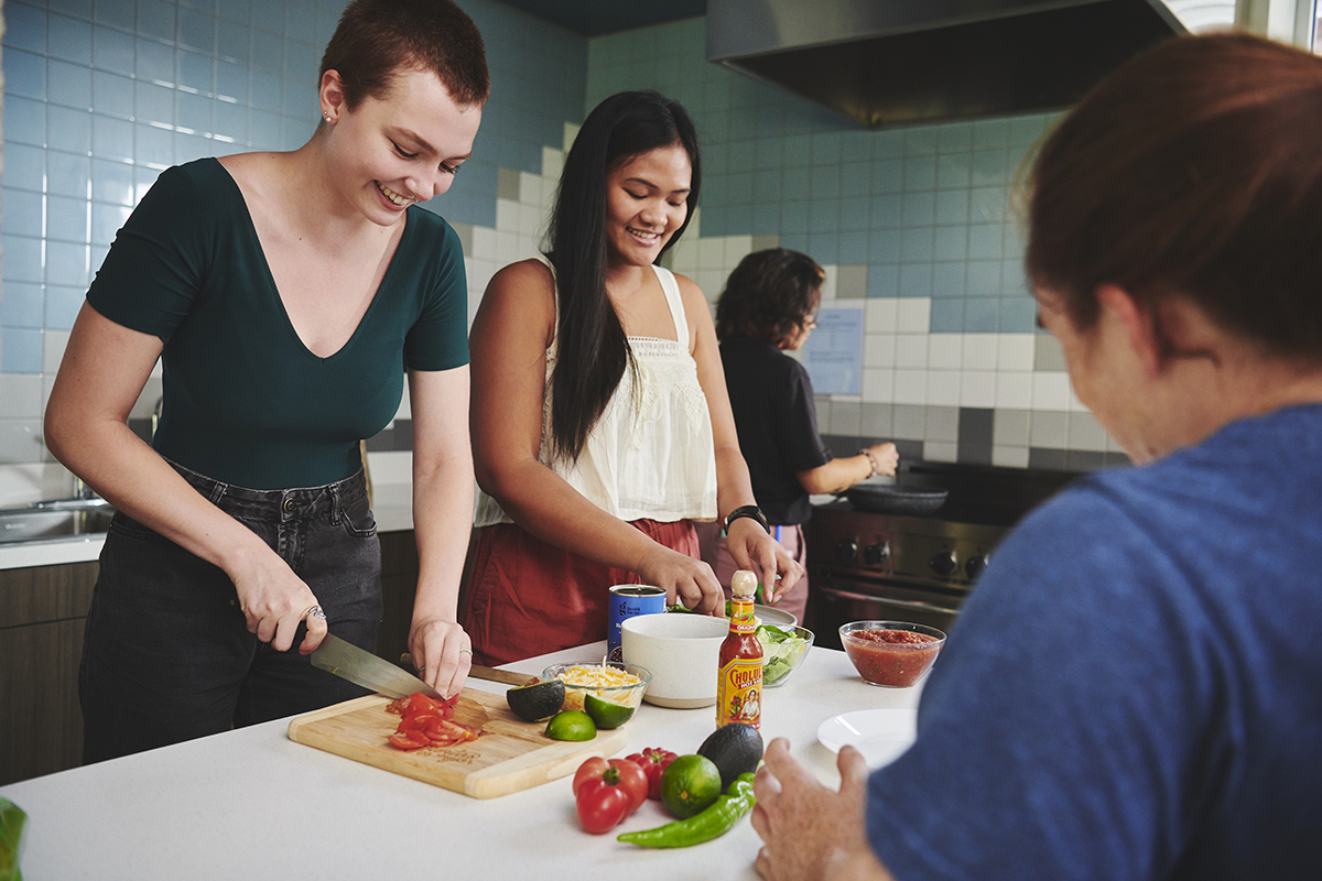 Four students working on a community meal with one cutting tomatoes