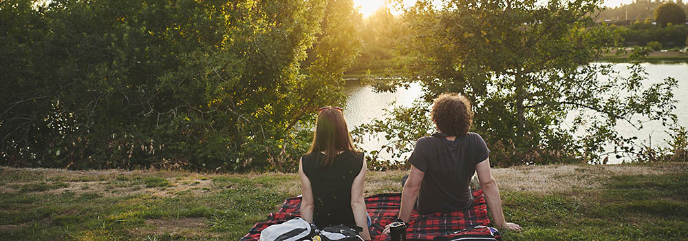 Two students sitting on a red plaid picnic blanket looking at the Willamette River at Riverfront Park