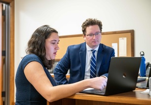 A student working with a law professional, both looking a laptop