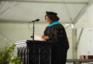 A commencement speaker standing in front of a microphone under a tent