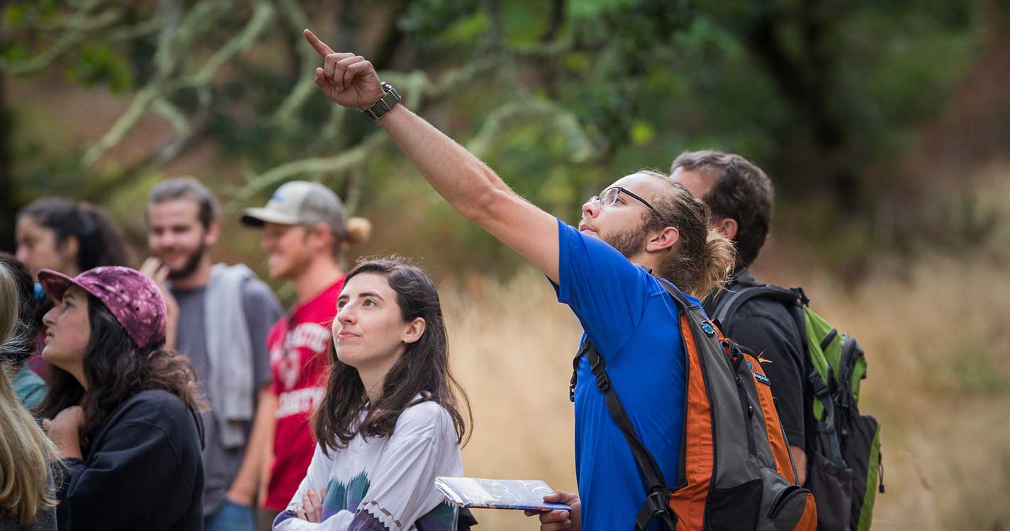 A student pointing up around a bunch of other students in nature