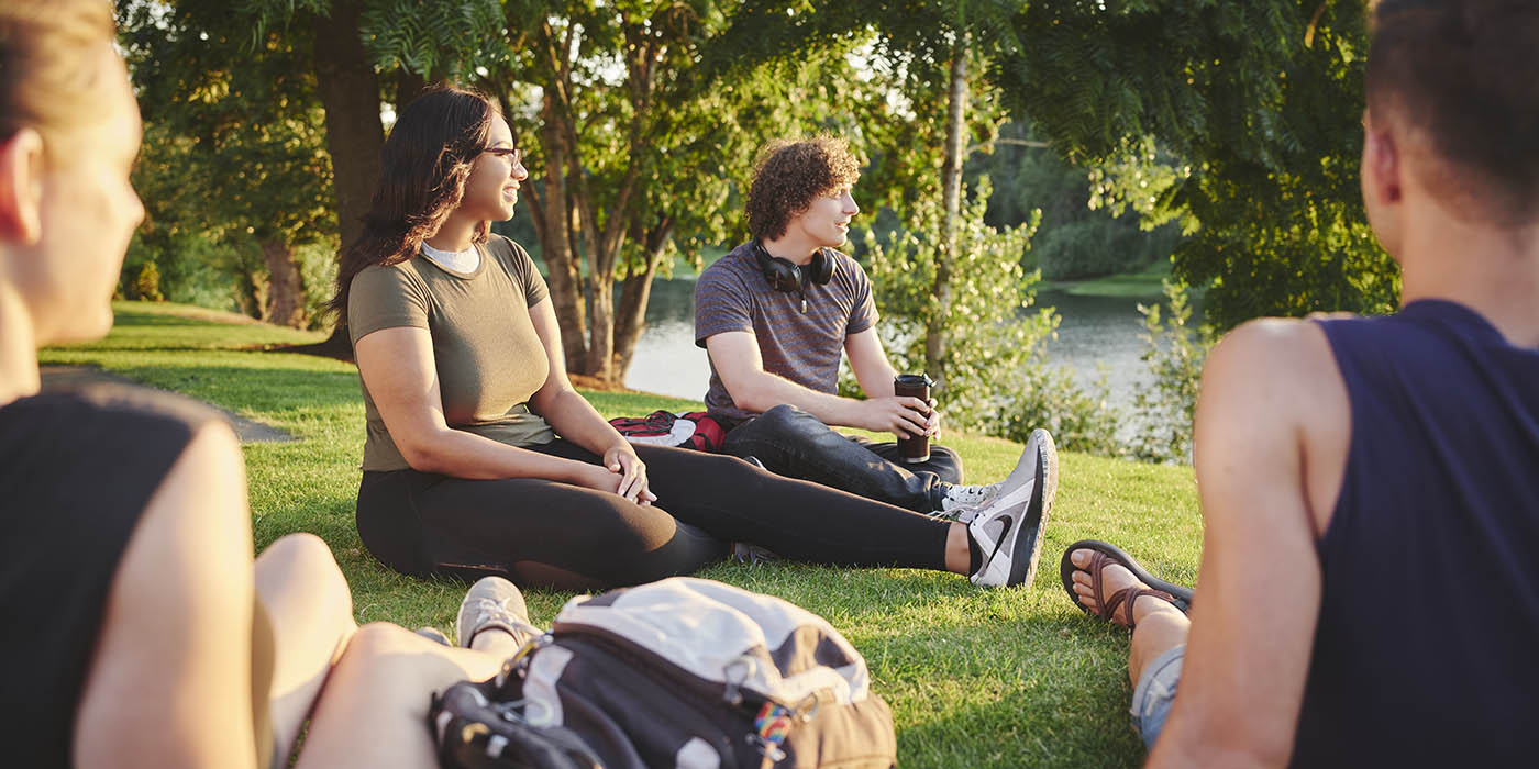 Four students sitting on grass at a park looking at the water.